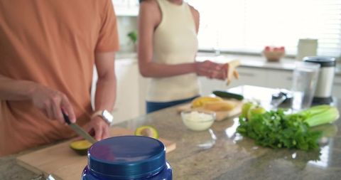 Couple preparing healthy breakfast on sunlit kitchen island with avocado and banana
