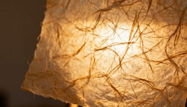 Glowing backlit fibrous paper lampshade revealing warm bulb glow and torn edge texture