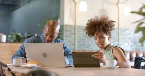 African american colleagues collaborating with laptop and tablet in modern cafe workspace