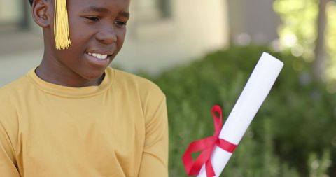 Young african graduate holding diploma with red ribbon celebrating achievement outdoors