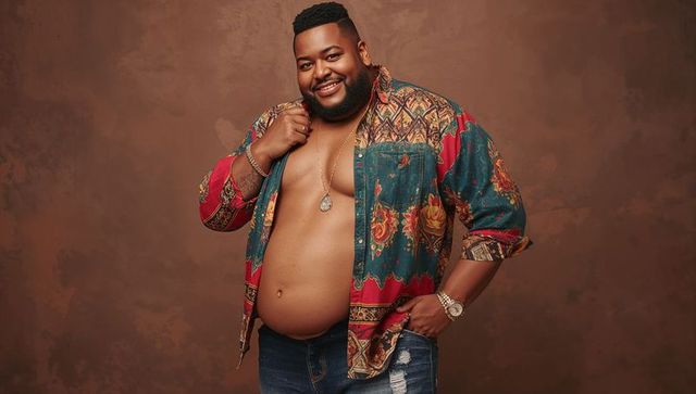 Confident plus-size male model wearing open patterned shirt and distressed jeans smiling