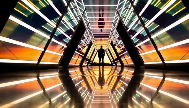 Silhouette man standing in futuristic glass corridor reflecting sunset, mirrored symmetry