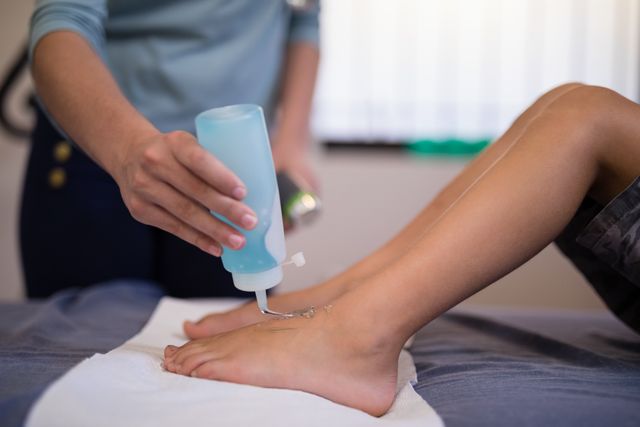 Therapist applying scanning gel on boy's feet in a hospital setting. Useful for healthcare, medical treatment, pediatric care, and wellness-related content.