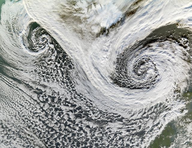 Impressive satellite image showing twin cyclones south of Iceland taken on November 20, 2006, by NASA's Terra satellite. Visible cloud formations demonstrate characteristic spiraling patterns of cyclones, which influence global weather. Ideal for educational materials, meteorological studies, and weather illustrations.