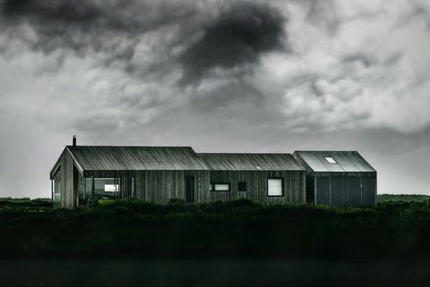 Minimalist coastal barn-style wooden house under dramatic stormy sky evoking solitude