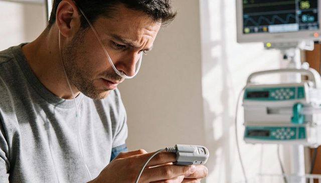 Male patient checking handheld pulse oximeter while receiving oxygen therapy in hospital