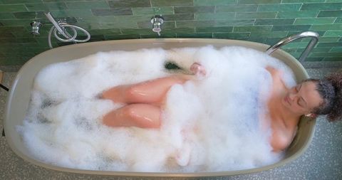 African american woman soaking in bubble bath, reclining in tub with green tile backdrop