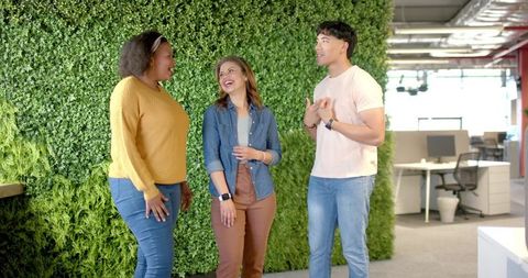 Diverse coworkers laughing and collaborating by living green wall in modern open office