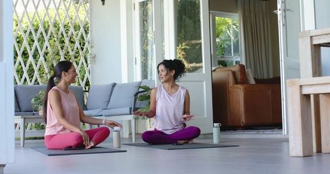 Diverse women practicing yoga on sunlit porch, sitting and chatting during mindful wellness
