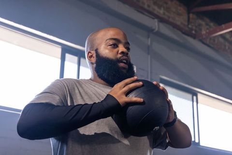 Bearded athlete holding medicine ball during indoor functional training with natural light