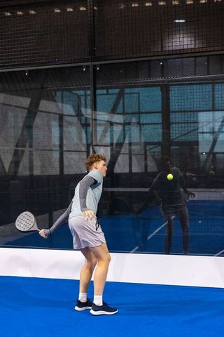 Young athlete swinging padel racket, hitting ball on indoor blue court during training