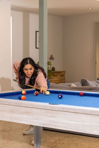 Asian woman playing pool on blue-felt table in cozy modern living room