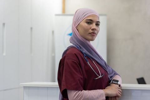 Confident muslim nurse standing at clinic counter wearing hijab and stethoscope