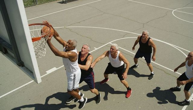 Senior men playing outdoor basketball reaching for rim on sunlit cracked court