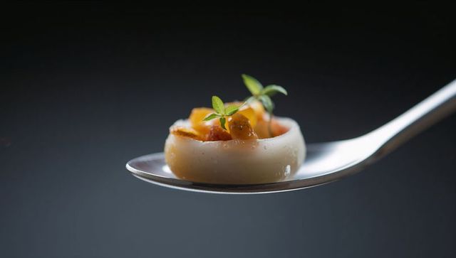 Minimalist gourmet canapé resting on silver spoon with diced orange and microgreens closeup