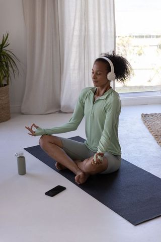 African american woman meditating at home with headphones on yoga mat practicing mindfulness