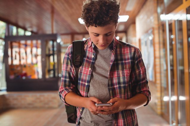 Schoolboy using mobile phone in corridor at school