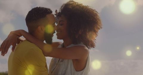Sunlit romantic couple embracing at golden hour with warm lens flare and intimate hug