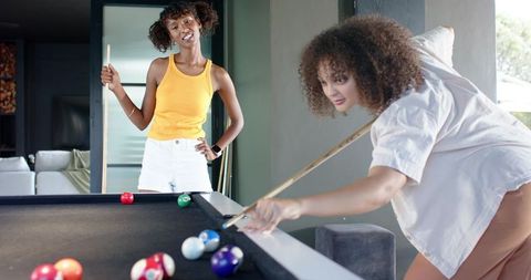Friends playing pool in modern home game room on black felt table with natural light
