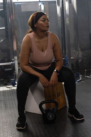 African american woman resting on plyo box after strength training wearing pink tank top