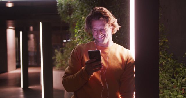 Smiling Man Using Smartphone with Earphones at Night in Urban Setting - Download Free Stock Images Pikwizard.com