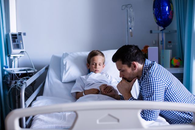 Father showing concern for his hospitalized son, sitting beside his bed in a hospital room. The scene reflects emotions of worry and care, highlighting the bond between parent and child. Useful for topics related to family, healthcare, medical treatment, parental care, and emotional support.