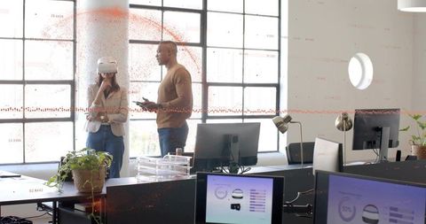Colleagues testing virtual reality prototype in bright industrial office with monitors