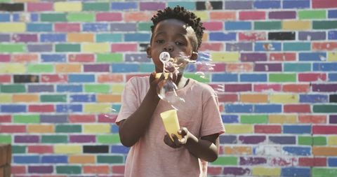Child blowing bubbles against colorful brick wall