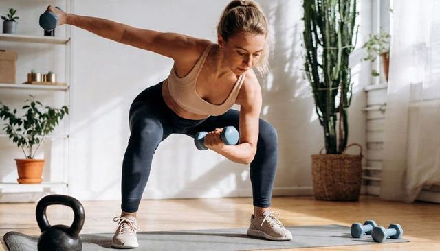 Home strength workout woman performing dumbbell squat row on mat in bright living room