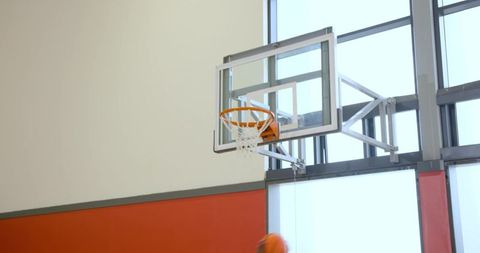 Mounted basketball hoop and glass backboard with blurred ball shooting toward net in gym
