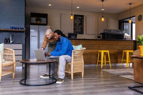 Barista helping customer with laptop in cozy coffeehouse collaborating on project