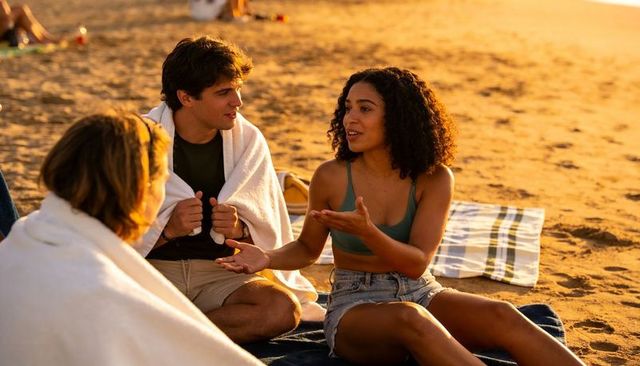 Friends chatting on golden sand during sunset gathering with towels and blankets