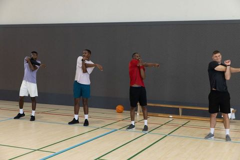 Diverse male teammates stretching arms during basketball warmup on indoor court