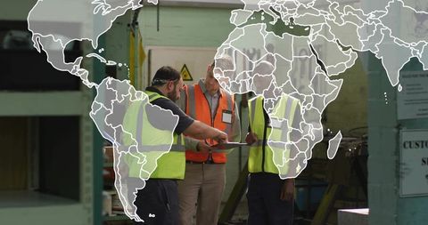 Factory team reviewing clipboard in high-visibility vests with translucent global map overlay