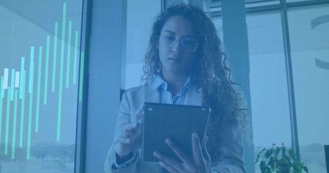 Standing businesswoman checking tablet with teal data chart overlay, corporate analytics