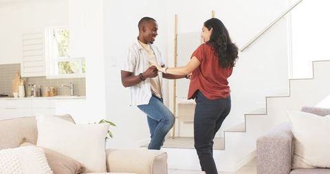 Couple dancing at home near staircase in sunlit minimal living room, casual joy, modern