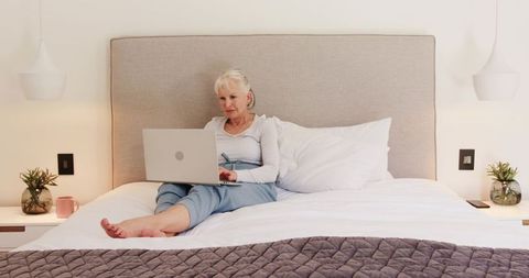 Senior woman relaxing with laptop on modern bed