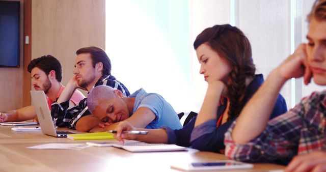 Group of students appearing distracted and uninterested during a classroom lecture. Useful for depicting lack of engagement in educational environments, illustrating classroom moments, or representing challenges in student concentration.