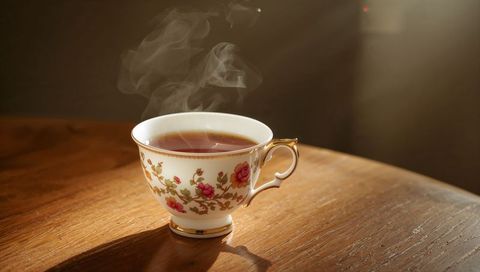 Steaming Vintage Floral China Teacup with Gilded Rim on Warm Sunlit Wooden Table