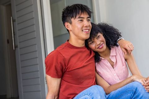 Interracial couple sitting on porch steps embracing and smiling, casual jeans and smartwatch