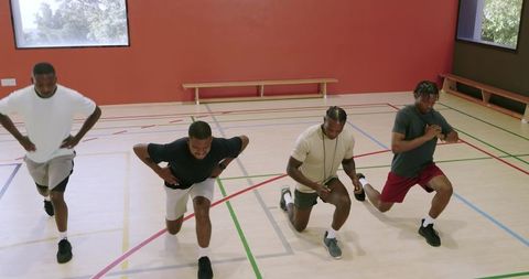 Group of men lunging in indoor gym following trainer for high-intensity cardio workout