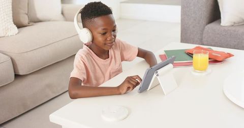 Child wearing headphones using tablet on stand for remote learning and home study