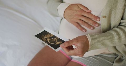 Pregnant Woman Holding Ultrasound Photo in Cozy Bedroom