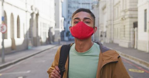 Man in Red Face Mask Walking on Urban Street