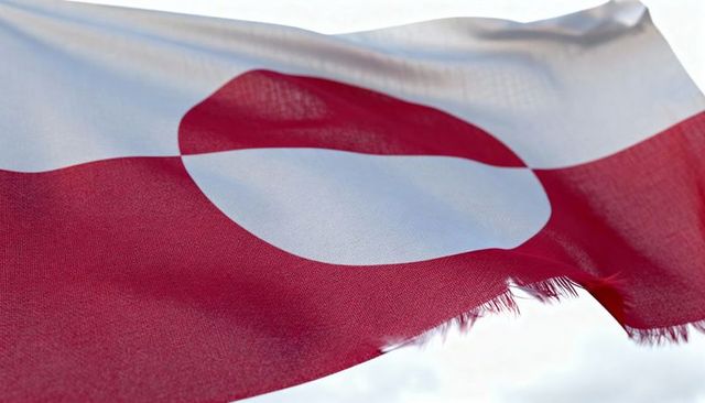 Waving greenland flag with frayed edge and bold red-and-white roundel in bright sky, fabric