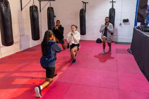 Multicultural training group performing lunges in boxing gym on red foam mats for strength