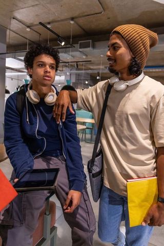 Diverse students collaborating over tablet in campus lounge wearing headphones