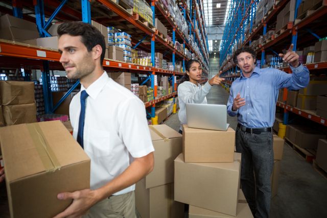 Warehouse manager carrying a box and his colleagues discussing in the warehouse