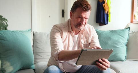 Middle-aged Man Relaxing at Home Using Tablet on Sofa