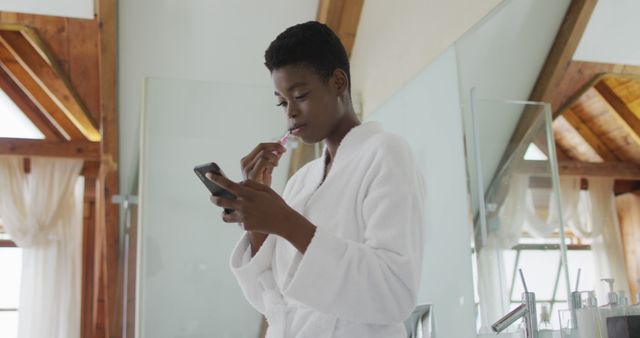 African american attractive woman brushing teeth and using smartphone in bathroom. beauty, pampering, home spa and wellbeing concept.